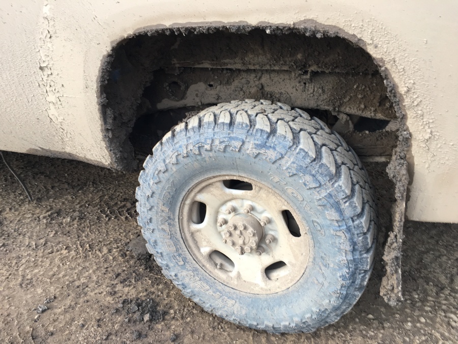 Close-up of a rugged light-duty commercial fleet truck tire completely encrusted in thick, heavy Alberta muskeg mud after operating on off-road terrain.