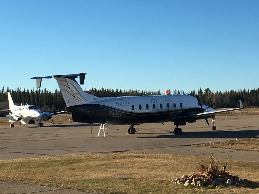 A North Cariboo Air twin-turboprop charter plane with a Canadian registration tail number parked on a remote northern Alberta airfield tarmac under a clear blue sky.