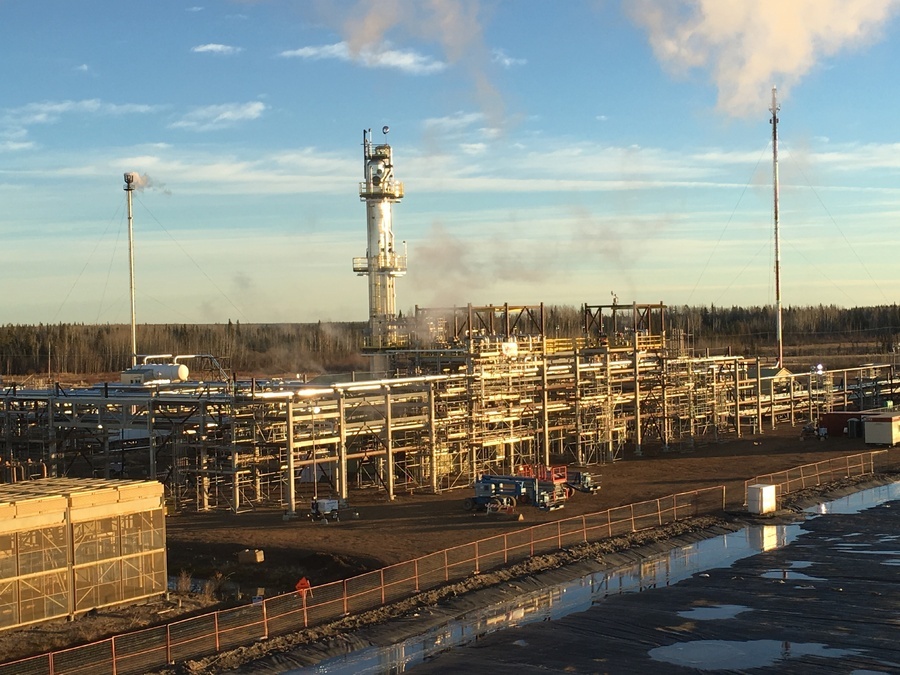 A sprawling industrial Liquefied Natural Gas (LNG) plant facility in northern Alberta, showcasing complex steel scaffolding, process piping, and emissions stacks venting steam into the horizon.