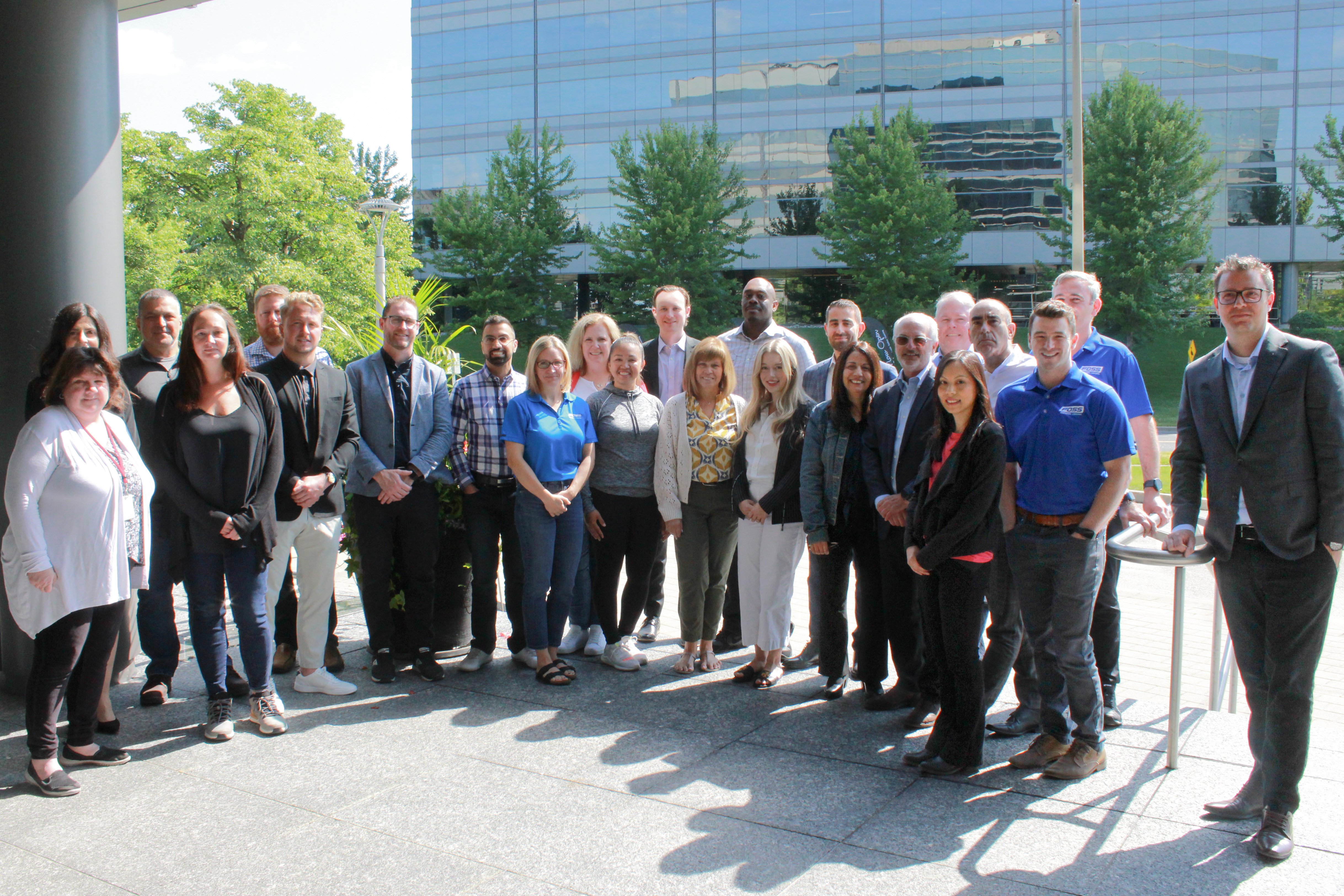 A group photo of Foss National Leasing employees standing outside a modern office building with glass windows on a sunny day.